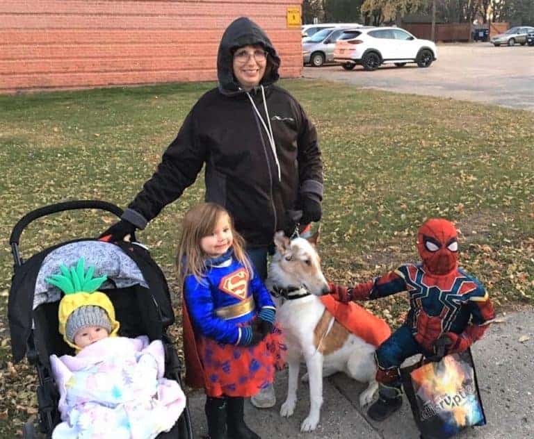 Veleda poses with Tag in Superdog cape/vest, Parker dressed as Spiderman, Lucy as Supergirl, and Ellie wearing a pineapple hat.