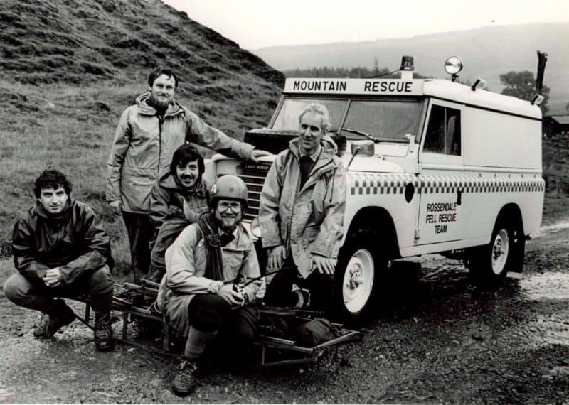 An old black and white photo showing rescue team members standing in front of an emergency vehicle.