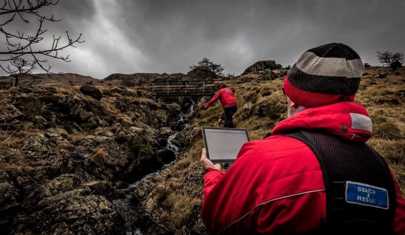 a handler works his dog through a stream-lined gully while an assessor takes notations on an electronic tablet