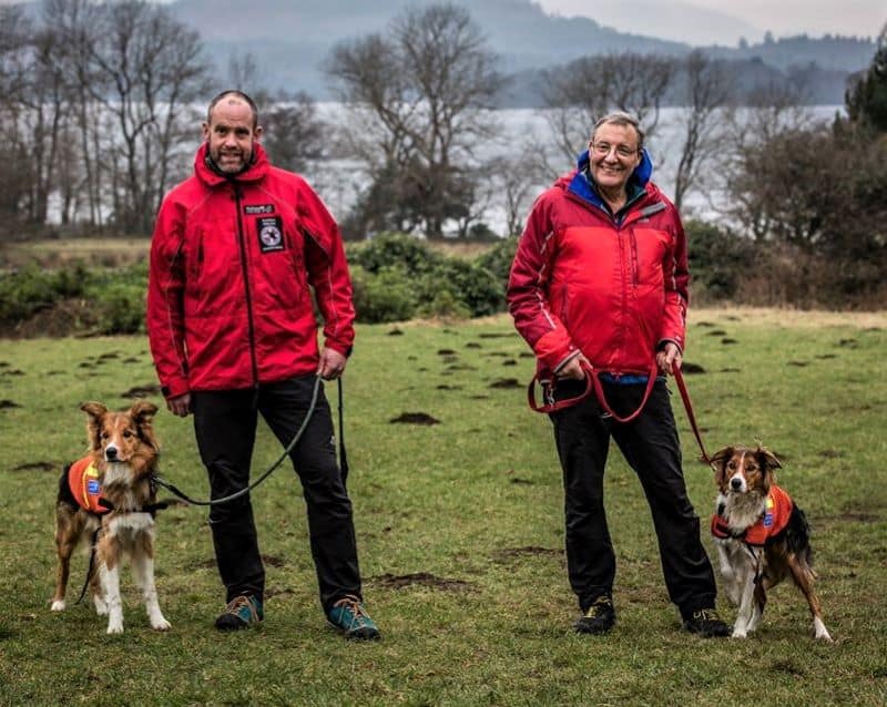 2 uniformed search and rescue dog handlers pose beside their search dogs