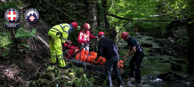 A group of rescuers lifting a person on a stretcher out of a riverbed area