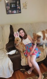 Isobel on the couch between Cory and Pixie. Isobel is hugging Cory, who is wearing bunny ears.