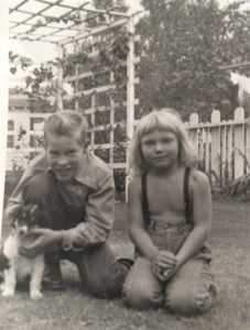 Black and white photo of a small tricolor Collie puppy posing outside with a smiling boy and younger girl wearing suspenders