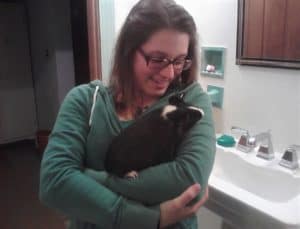 brunette girl holding a black and white guinea pig in her arms