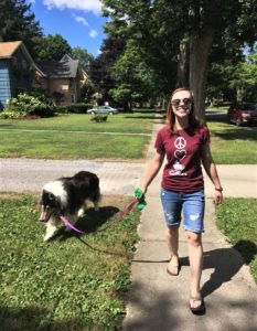 Brianna walks down a sidewalk smiling while Pepsi walks beside her on a leash