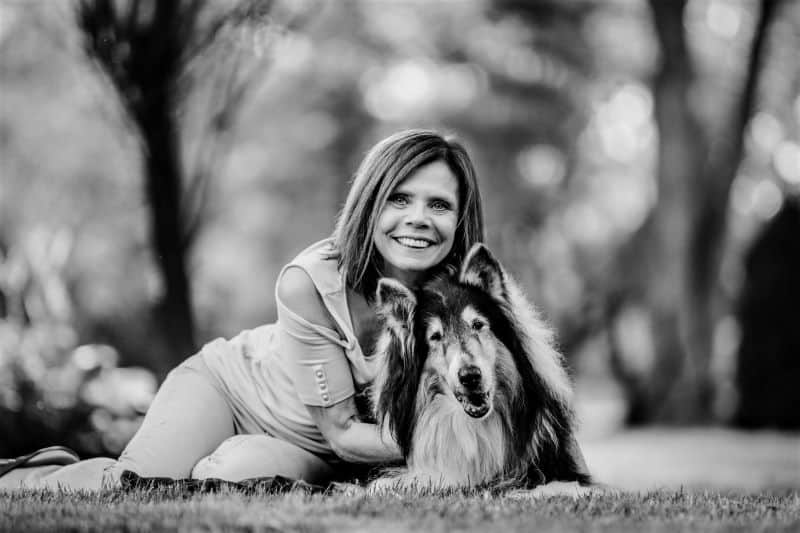 Pepsi lies on the grass smiling happily next to Brianna's mom, who has her arms around him and is also smiling happily