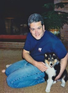 Pepsi as a puppy indoors sitting on the floor next to Dad, getting a big hug from him