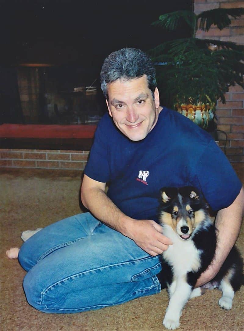 Pepsi as a puppy indoors sitting on the floor next to Dad, getting a big hug from him