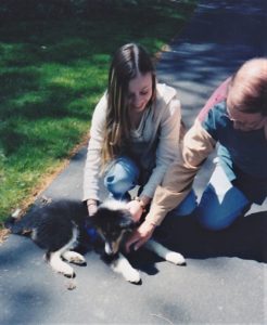 Brianna and Grandpa kneel on the ground to pet Pepsi as a small puppy