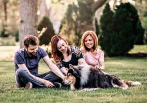 Pepsi lies on the grass being petted and adored by Pat, Brianna, and Brianna's mom