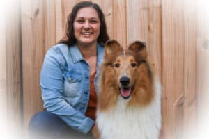 A girl in a jean jacket kneels outside in front of a fence next to a sable merle and white Rough Collie