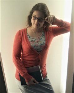 A girl wearing glasses and very modest attire holds a book