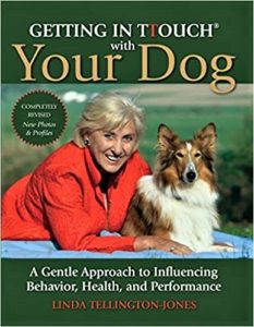 Book cover says "Getting in T-Touch with Your Dog" and shows a woman lying down on the ground outside next to a sable and white Rough Collie