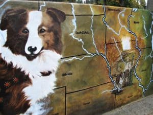 A mural painted on a wall depicts a sable and white Collie over a map, with a smaller painting of the same Collie with a man in a hat